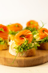 Canapes with mozzarella cheese, salad, salmon and pea sprouts, toast with red fish on a wooden board close up