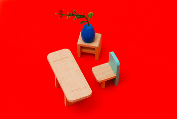 Wooden toys on a red paper background. One blue-backed toy chair, table, bedside table and flowerpot
