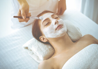Beautiful brunette woman enjoying applying cosmetic mask with closed eyes. Relaxing treatment in medicine and spa concepts