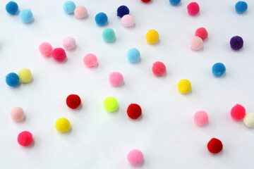 Small fur balls randomly lie on a white background. Pompoms for needlework and handmade. - obrazy, fototapety, plakaty