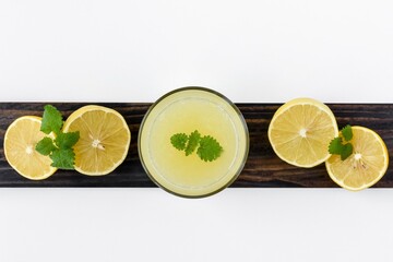A glass with freshly squeezed lemon juice and lemon balm leaves on an old wooden board. White background. Top view. Place for your text.