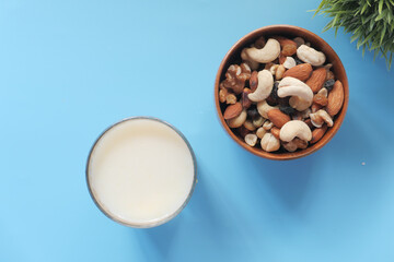 many mixed nuts in a bowl and glass of milk on blue background 