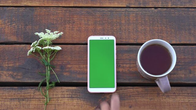 Closeup top view flatlay 4k video of modern smartphone laying on brown wooden surface. Screen of device with empty blank green color.