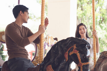 couple asian man and woman dating and riding on horse at Carousel amusement park. Concept happy and...