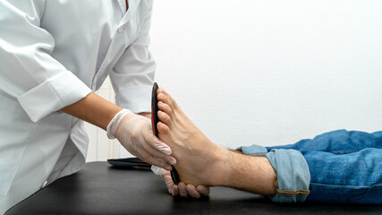 Obraz na płótnie Canvas Close-up of a podiatrist trying out insoles on a patient. You can see the podiatrist's hands and the patient's foot on the table against a white background