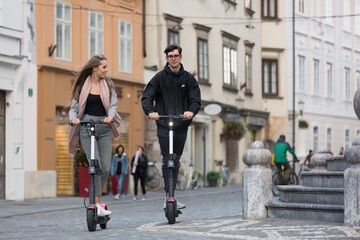 Trendy fashinable teenagers riding public rental electric scooters in urban city environment. New eco-friendly modern public city transport in Ljubljana, Slovenia.