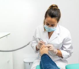 Frontal view of a young chiropodist doing chiropractic work in her podiatry clinic. The chiropodist is filing the patient's nails with a hand polisher
