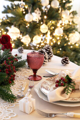 Christmas or new year table setting with ivory cloth ,ribbon, hypericum berry, evergreen leaf and pinecone. Christmas tree background.