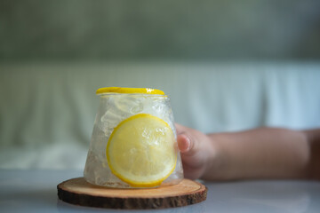 Child hand with a glass ice cubes and slices of lemon in front.