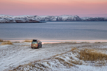 The car is parked on the shore of the Arctic ocean. Travel concept of traveling by car. Amazing view of the Northern Bay in the village of Teriberka