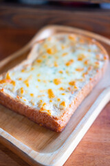 A piece of sliced bread toast with cheese served in wooden plate