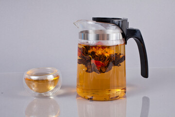 Exotic green flower bud tea in a glass tea pot on a gray background.