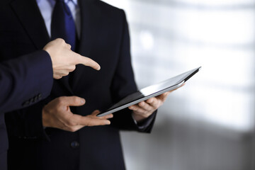 Business people use a tablet computer for discussion of their new project, standing in a modern office. Unknown businessman or male entrepreneur with a colleague at workplace. Teamwork and partnership
