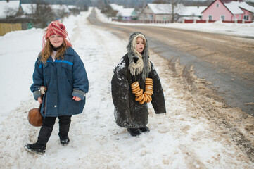 Two beautiful village girls stand on the road with balalaika and barankas in winter