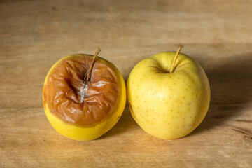 Two yellow golden apples, one rotten and one fresh, on wodden board.