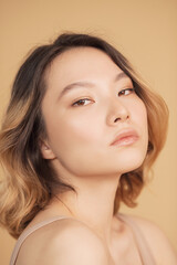 Naklejka premium Concept beauty and fashion of face and body skin. Profile young girl of Asian appearance with wavy streaked hair on beige background