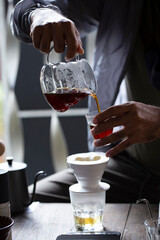 Black coffee pours from a jug into a glass close up