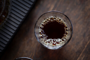 Black coffee pours from a jug into a glass close up