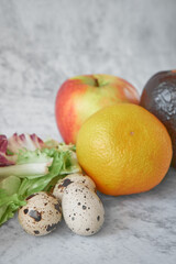 Quail eggs, lettuce leaves, mandarin, apple, avocado on a gray concrete background. Healthy food for getting vitamins to strengthen immunity. Healthy lifestyle, cooking concept.