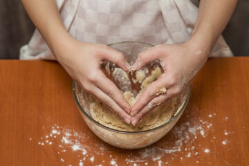 Heart from hands. A girl kneads cookie dough in her kitchen. Homemade baking.