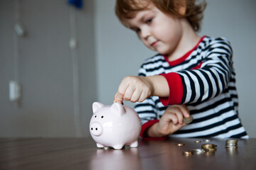 Cute baby preschooler puts money in the piggy Bank.