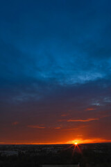 Dramatic sunset during autumn season with dark blue cloudy sky and bright orange and yellow horizon.