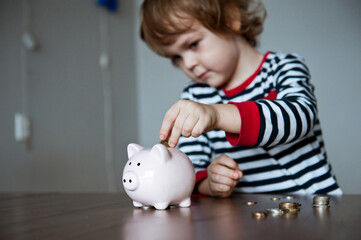 Cute baby preschooler puts money in the piggy Bank.