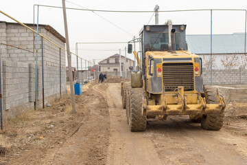 Fototapeta na wymiar Construction site of a new road and sidewalk in the city. Yellow tractor and road roller.