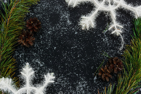 Winter template. Natural frame made of green pine branches, pine cones and artificial snowflakes on black background covered with snow with space for text. Copy space. Mockup. Flat lay