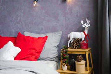 Christmas decor in the bedroom. White deer with red scarf and bumps by the bed