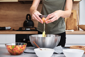 Woman in kitchen cooking a dough. Hands breaks an egg into a bowl