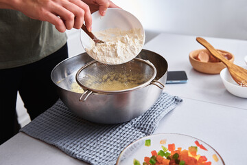 Woman in kitchen cooking a dough. Hands pour flour into a bowl