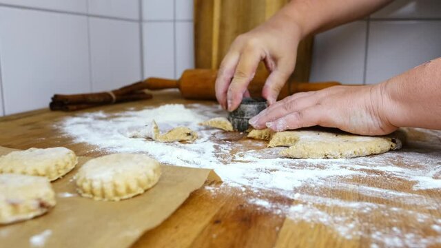 woman prepares butter cookies at home in the kitchen, the table is sprinkled with flour, rolls out the dough, cuts out the shape, the concept of cooking festive food, christmas sweets