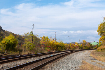 Fototapeta na wymiar Sweeping view of railroad tracks running into the distance with seasonal fall colors, blue sky and clouds, horizontal aspect