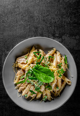 Penne pasta with chicken meat, cream sauce and cheese in a bowl on Dark grey black slate background
