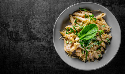 Penne pasta with chicken meat, cream sauce and cheese in a bowl on Dark grey black slate background