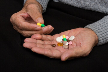 An elderly man holds a lot of colored pills in old hands. Painful old age. Health care of older...