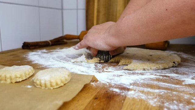 woman prepares butter cookies at home in the kitchen, the table is sprinkled with flour, rolls out the dough, cuts out the shape, the concept of cooking festive food, christmas sweets