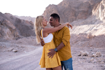 Blond woman and man hug each other. Two people, lovely romantic couple wear mustard, yellow clothes look face to face and kiss. Outdoor on brown background.  - Powered by Adobe