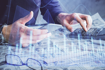 Double exposure of man's hands holding and using a digital device and forex graph drawing. Financial market concept.