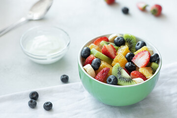 fruit salad in a green salad bowl with white yogurt on a white background