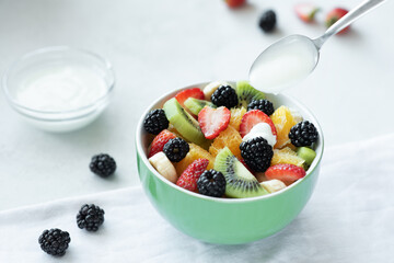 fruit salad in a green salad bowl with yogurt in a spoon on a light background