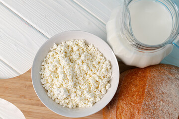 Glass jar of milk, bowl of cottage cheese and bread on wooden table