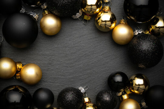 Holiday winter background. Gold Christmas baubles decoration on black textured background. Winter festive composition with copy space.