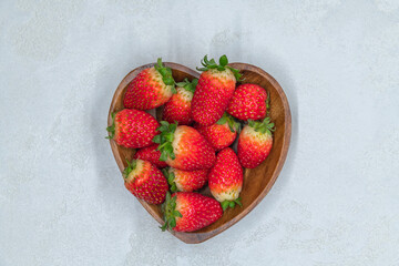 Fresh red strawberries in heart shaped wooden bowl top view. Strawberry fruits on gray concrete...