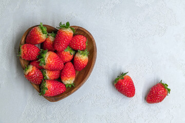 Fresh red strawberries in heart shaped wooden bowl top view. Strawberry fruits on gray concrete background. Copy space for your text. Valentine's day theme.