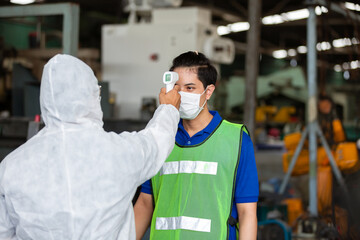 Factory workers in white protection suit disinfecting using infrared forehead thermometer scan at...