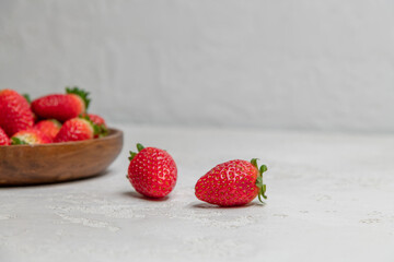 Side view of fresh red strawberries lying on gray concrete background next to wooden bowl full of strawberry fruits. Selective focus. Copy space for your text. Organic food theme.