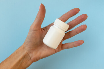 Hand hold white bottle for pills on a blue background.