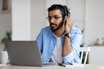 Focused Indian Guy In Headset Watching Webinar On Laptop At Home